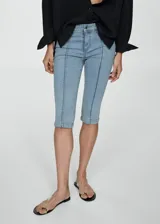 Jeans capri de corte skinny y tiro medio, confeccionados en tejido denim de algodón con elastano. Presentan costuras decorativas verticales en el frente, cierre de cremallera con botón, trabillas y bolsillos funcionales.