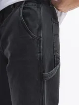 Jean estilo carpintero de corte oversized, color negro lavado, con múltiples bolsillos funcionales y presillas laterales.