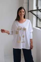Remera blanca de corte holgado y manga larga, con estampado floral en color dorado en el frente.