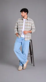 Camisa de manga larga con estampado de cuadros en tonos beige, marrón y azul claro. Presenta cuello clásico, cierre frontal con botones y un pequeño logo bordado en el pecho.