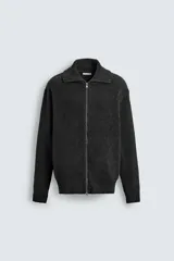 Chaqueta de punto con textura acanalada, cuello subido y cierre frontal completo con cremallera metálica. Presenta un corte relajado y acabados en rib en puños y ruedo.