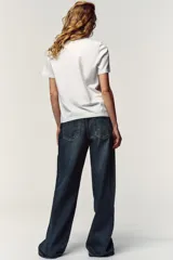 Camiseta blanca de manga corta y cuello redondo, con aplicación de organza y texto negro a contraste en el pecho.