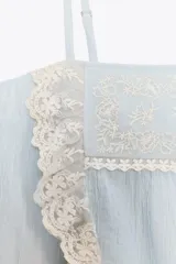 Top celeste con tirantes finos ajustables y escote recto. Detalle de puntilla y bordado floral en el frente.