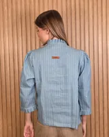 Camisa de algodón color blanco con rayas verticales rosadas, cuello alto con volados, mangas tres cuartos abullonadas con puños elastizados con volados y cierre frontal de botones oscuros.