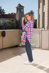 Camisa a cuadros grandes en tonos rosa, blanco y azul. De corte amplio, con cuello clásico, mangas largas con puños abotonados y bajo irregular con aberturas laterales.