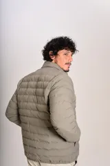 Campera puffer de corte clásico en color beige, con cierre frontal, cuello alto y puños elásticos. Presenta un diseño acolchado horizontal y un pequeño logo bordado en el pecho.