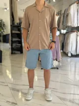 Camisa de manga corta color blanco marfil, confeccionada en tejido texturizado con cuello camisero, cierre frontal de botones y un pequeño bordado oscuro en el pecho.