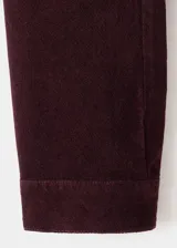 Chaqueta entallada de terciopelo bordó, de manga larga con puños abotonados, cuello camisero, cierre frontal con botones y detalle de costuras visibles.