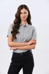 Camisa celeste rayada de manga corta, con cuello camisero y cierre frontal con botones. Presenta un corte entallado y un pequeño detalle de placa metálica en el borde inferior.