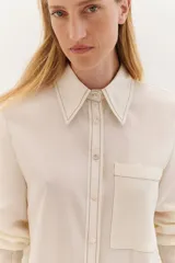 Camisa color crema de lyocell con cuello clásico, cierre frontal con botones, bolsillo de parche en el pecho y pespuntes a contraste en negro.