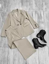 Conjunto sastrero de color beige compuesto por un blazer oversize de doble botonadura con bolsillos con solapa y un pantalón de vestir de corte recto y pernera ancha.