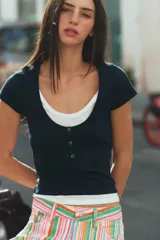 Camiseta efecto doble en color crudo y blanco, de manga corta y corte slim fit. Cuenta con escote redondo, cierre frontal parcial con botones a presión y diseño de capas superpuestas.
