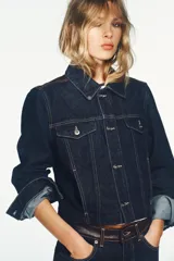 Cazadora de corte cropped confeccionada en tejido denim azul oscuro, con cuello solapa, cierre frontal de botones metálicos y bolsillos con solapa en el pecho. Presenta detalles de aplicación en piel a contraste en la zona de los hombros.