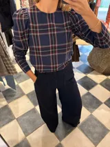 Blusa azul marino con estampado de cuadros en tonos rojo, blanco y negro. Tiene cuello redondo y mangas largas abullonadas.