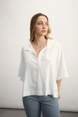 Blusa negra de corte holgado con cuello polo y cierre frontal parcial. Presenta mangas cortas amplias y un diseño minimalista.