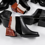 Bota corta de cuero vacuno con diseño tricolor, combinando paneles en negro, blanco y cuero texturizado efecto reptil en tono marrón. Presenta taco cuadrado forrado, punta cuadrada y cierre lateral interno.