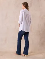 Camisa blanca de lino con cuello con solapa, manga larga regulable con presilla y botón, y abertura central con botones.