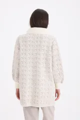 Saco de paño con textura jaspeada en tonos beige y visón, con cuello redondo y cierre frontal con botones a presión. Presenta mangas largas con puños tejidos en color crema y detalles de piel sintética en el cuello.