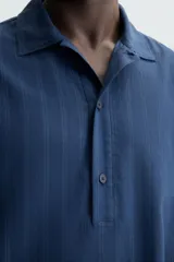 Camisa polo de manga larga con cierre frontal de botones, confeccionada en tejido con textura de rayas verticales sutiles.