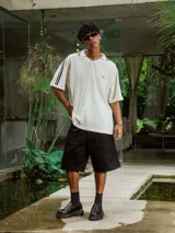 Chomba de tejido de punto cerrado color blanco, con cuello polo y mangas cortas. Presenta un bordado sutil en el frente y tres franjas negras en los hombros.