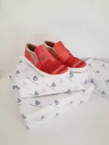 Zapatillas de cuero de diseño artesanal y color rojo con detalles pintados a mano por Carolina De Cunto. Presentan combinaciones de texturas, detalles dorados y suela de goma blanca.