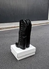 Botas de caña alta negras con punta en pico, taco bajo y detalles metálicos plateados en los laterales de la caña.