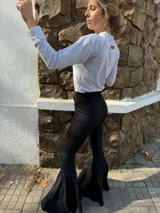 Pantalón negro de tiro alto con corte acampanado y terminación en volado en el ruedo.