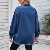 Campera tipo sobrecamisa de denim en tono azul claro, con corte oversize, cuello italiano, cierre frontal con botones metálicos, bolsillos frontales con solapa y ruedo con detalle desflecado.