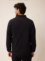 Sweater de polar negro con cuello alto y cierre frontal parcial. Presenta mangas largas con puños elásticos y un pequeño logo bordado en el pecho.