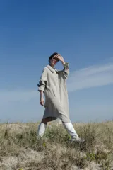 Tapado amplio color gris claro, confeccionado en lana fina sin teñir. Tiene hombros caídos, mangas largas con presillas y detalle de color en el cuello.