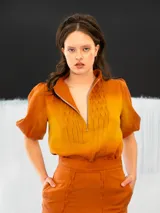 Blusa color ocre de algodón tipo seda, teñida a mano con técnica tie dye. Tiene corte recto, cierre invisible en el escote delantero y mangas regulables con elástico.