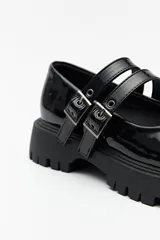 Guillerminas negras de cuero sintético charolado, con plataforma chunky y doble tira ajustable con hebillas metálicas.