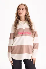 Buzo deportivo sin friza a rayas anchas en tonos blanco y tostado, con cuello polo, escote en V y estampa frontal con la inscripción "California est.1969" en color fucsia. Presenta un corte semi oversize y mangas largas.