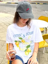 Remera oversize blanca de algodón con cuello redondo y hombros caídos. Estampado frontal con ilustración de dos vasos de limonada, limones y texto "CITRIC & SOUR".