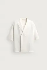 Camisa de corte relaxed fit confeccionada en tejido fluido mezcla de viscosa y lino, color blanco crudo. Presenta diseño de doble botonadura, cuello con solapas de muesca y manga corta.