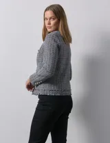 Chaqueta Nanette de tejido tweed color beige, con cuello a la base, abertura central y bolsillos delanteros. Tiene apliques de botones perlados en los puños, terminación desflecada y forro interno.