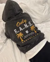 Hoodie de felpa suave color negro con efecto acid wash y corte oversize, con capucha y estampa gráfica en la espalda con diseño de palmeras y texto.