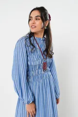 Vestido largo a rayas verticales azules y blancas, con manga globo y diseño de nido de abeja con hilo elástico hasta la cintura. Cuello alto fruncido y falda amplia con caída fluida.