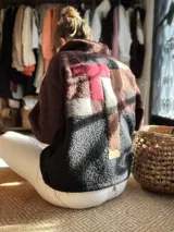 Buzo de lana uruguaya con diseño patchwork geométrico inspirado en el Tetris. Presenta una combinación de texturas y colores en tonos marrón, negro, rojo y gris, con una etiqueta de cuero en la parte inferior trasera.