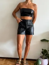 Short negro de cuero sintético con textura crocco, tiro alto, corte ajustado, bolsillos laterales y cierre frontal con botón.