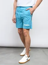 Bermuda deportiva celeste de piqué con cordón ajustable en la cintura, bolsillos laterales y logo Umbro estampado en blanco en la pierna izquierda.