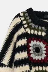 Chaqueta de punto con cuello redondo y manga larga, que combina un diseño de rayas horizontales en blanco y negro con paneles frontales decorados con motivos de crochet en tonos tierra y granate. Presenta cierre frontal con botones.