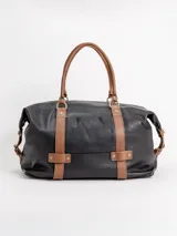 Bolso de viaje grande de cuero marrón con detalles en cuero negro, doble asa de mano y tiras decorativas verticales.