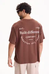 Remera oversize de manga corta en color marrón, confeccionada en 100% algodón. Presenta un diseño gráfico estampado en la espalda con inscripciones en color blanco.