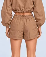 Conjunto deportivo de dos piezas color durazno, compuesto por un buzo cropped de manga larga con cuello alto ajustable y cintura regulable, y un short con cintura clochard y cordones laterales.