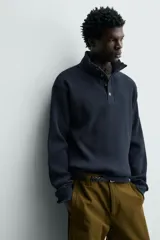 Sudadera de corte relajado confeccionada en tejido de algodón con textura waffle. Presenta cuello subido con cierre frontal de cuatro botones y mangas largas con puños y ruedo en rib.