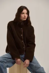 Campera de corderito color marrón, con cuello alto, cierre frontal con botones y terminaciones con ribete al tono.
