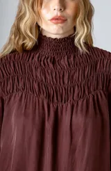 Blusa negra de manga larga con cuello alto fruncido y diseño amplio con frunces en la parte superior.