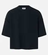 Remera negra de algodón con corte oversized, cuello redondo y manga corta. Presenta un tejido acanalado y un dobladillo sin rematar.