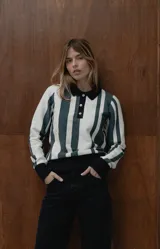 Buzo tipo polo de punto de algodón con diseño de rayas verticales en blanco y gris oscuro. Presenta cuello camisero negro, cierre frontal con botones y puños negros en las mangas y en el ruedo.